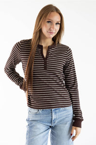 A woman modeling a brown and white horizontally striped long-sleeve henley shirt with a split button placket, paired with light blue jeans, against a plain white background.