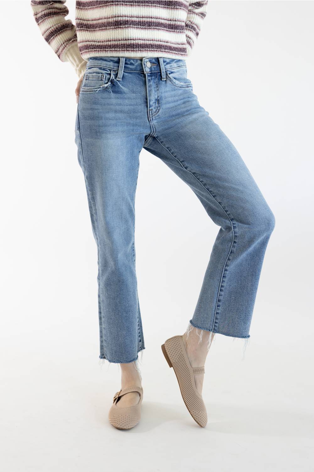 A person wearing light blue cropped jeans with a straight-to-medium leg, paired with a striped knit sweater and beige loafers, shown against a plain white studio background.