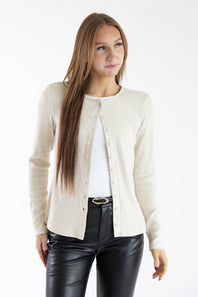 A woman modeling a cream ribbed knit cardigan over a white top and black faux-leather pants, photographed against a plain white studio background.