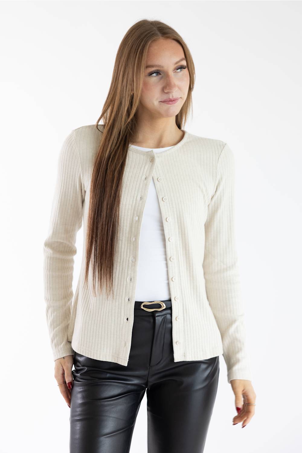 A woman modeling a cream ribbed knit cardigan over a white top and black faux-leather pants, photographed against a plain white studio background.