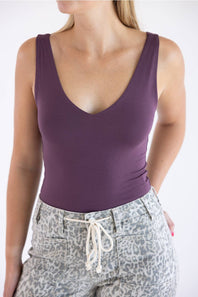 A woman wearing a sleeveless deep V-neck tank top in a muted plum purple, paired with gray leopard-print pants with a cream drawstring, against a plain white background.