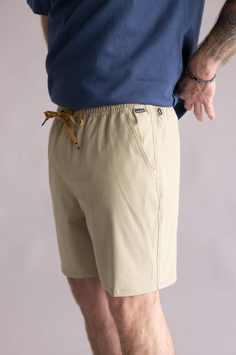 Side view of a person wearing beige shorts and a blue shirt against a plain background