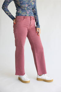 A model wearing a pair of dusty rose straight-leg jeans, styled with a blue floral long-sleeve top and white platform sneakers, photographed against a plain white studio background.