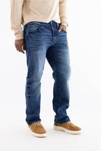 Front three-quarter view of a model from the waist down wearing medium-wash straight-leg blue jeans with whiskering at the hips, paired with a cream waffle-knit sweater and tan suede slip-on sneakers against a plain white background.