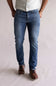 Person wearing blue jeans and brown shoes on a plain background. The jeans are Weatherproof Vintage Slim Jeans for Men in Tidepool Tint.