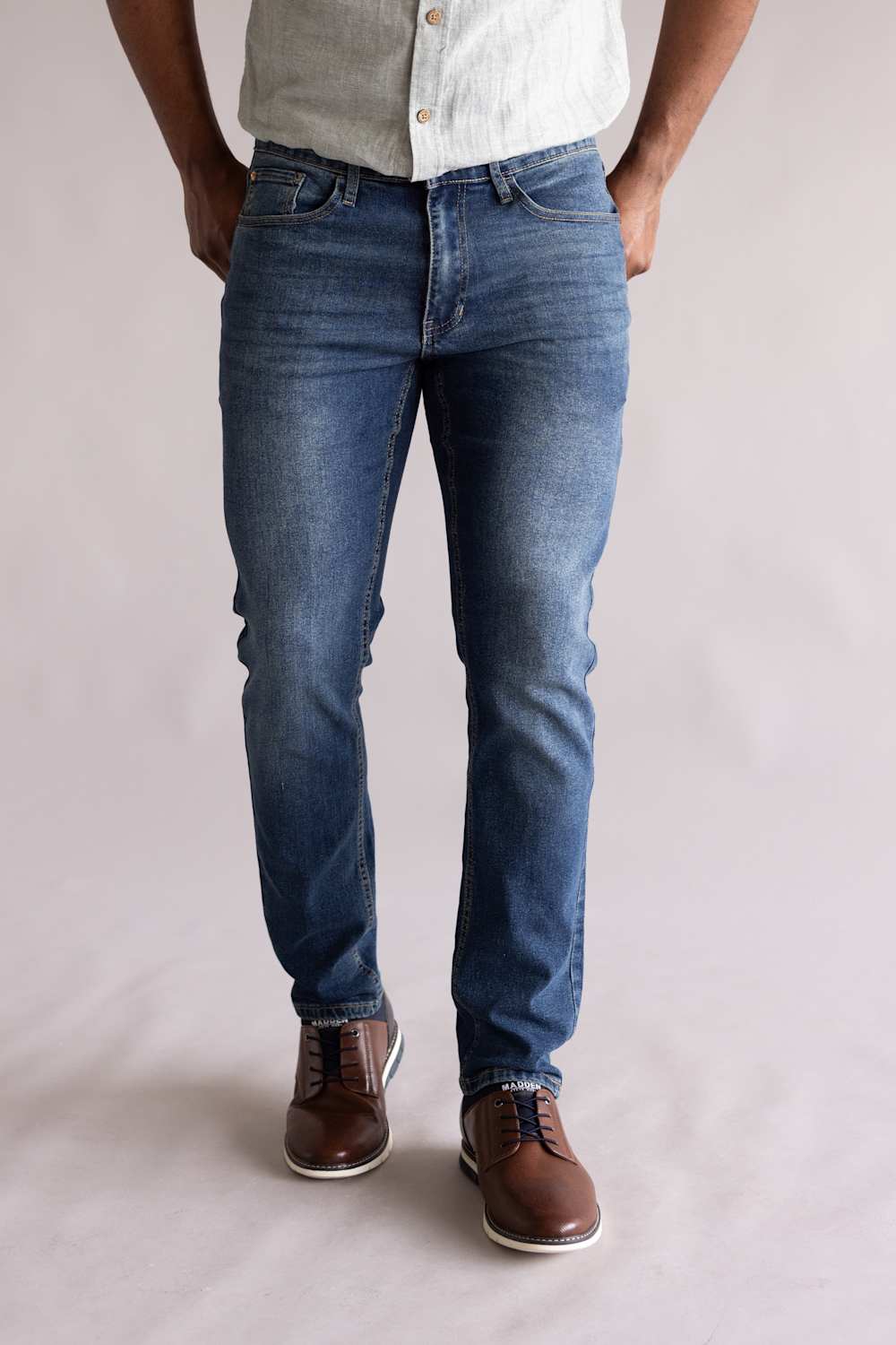 Person wearing blue jeans and brown shoes on a plain background. The jeans are Weatherproof Vintage Slim Jeans for Men in Tidepool Tint.