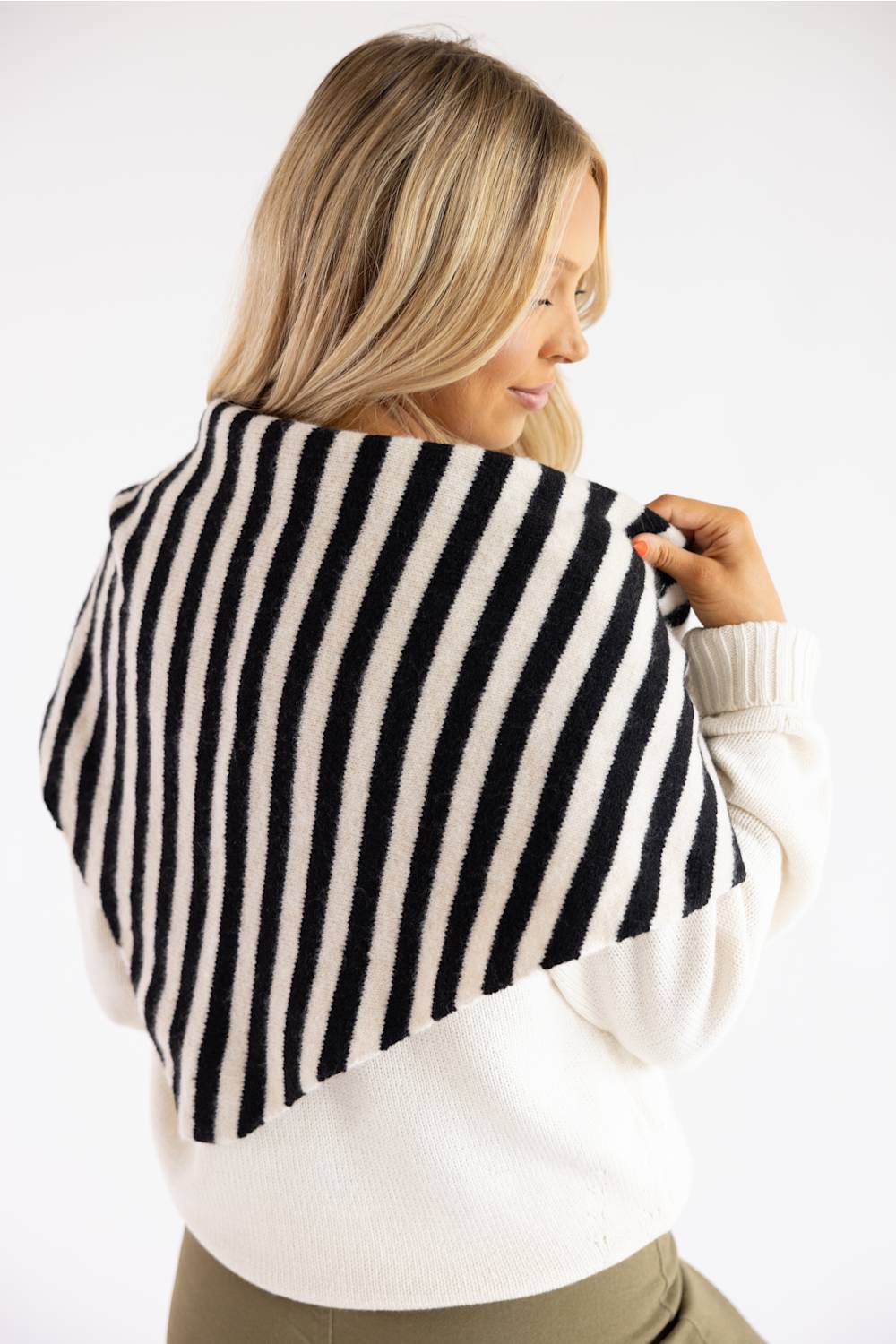 A woman with blonde hair is shown from behind wearing a black and off-white vertically striped knit shawl draped over her shoulders, paired with a white sweater.