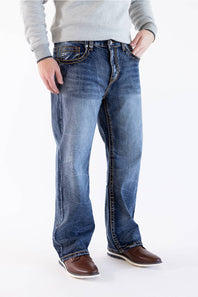 Side profile view of Men's True Luck Truman Loose Straight jeans in a dark wash, emphasizing the relaxed straight-leg silhouette, distinct fading along the thighs and shins, and styled with a gray sweater and brown shoes.