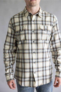 Close-up front view of a male model wearing the Split Flannel Shirt for Men in Grey Ecru, showcasing the beige, gray, and brown plaid pattern, dual buttoned flap chest pockets, long sleeves, and button-down front against a neutral gray background.