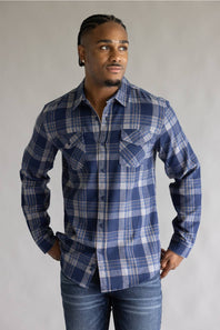 Front view of a model wearing the Split Men's long-sleeve flannel shirt in a navy blue, khaki, and white plaid pattern, featuring two button-flap chest pockets, styled with blue jeans against a grey studio background.