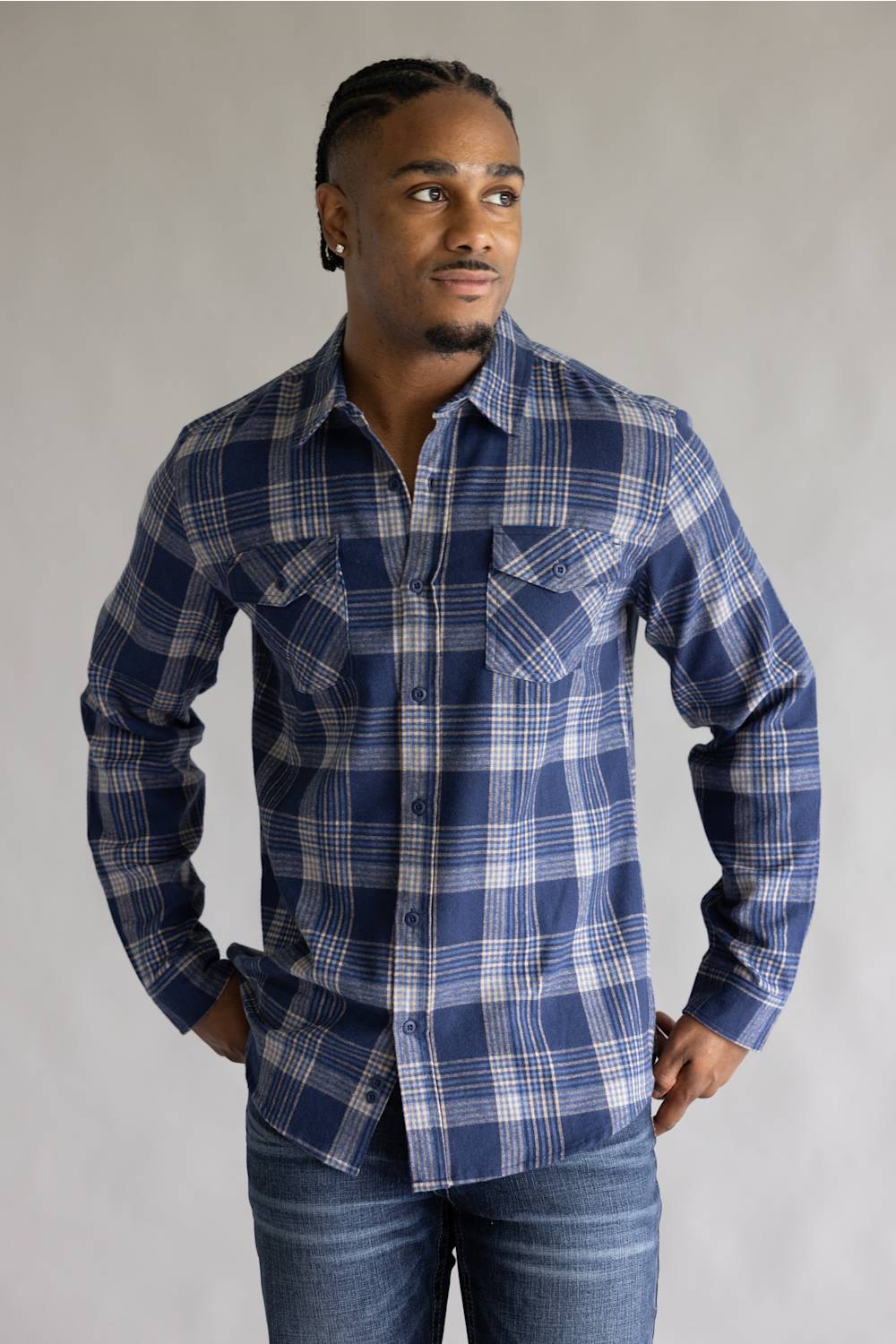 Front view of a model wearing the Split Men's long-sleeve flannel shirt in a navy blue, khaki, and white plaid pattern, featuring two button-flap chest pockets, styled with blue jeans against a grey studio background.