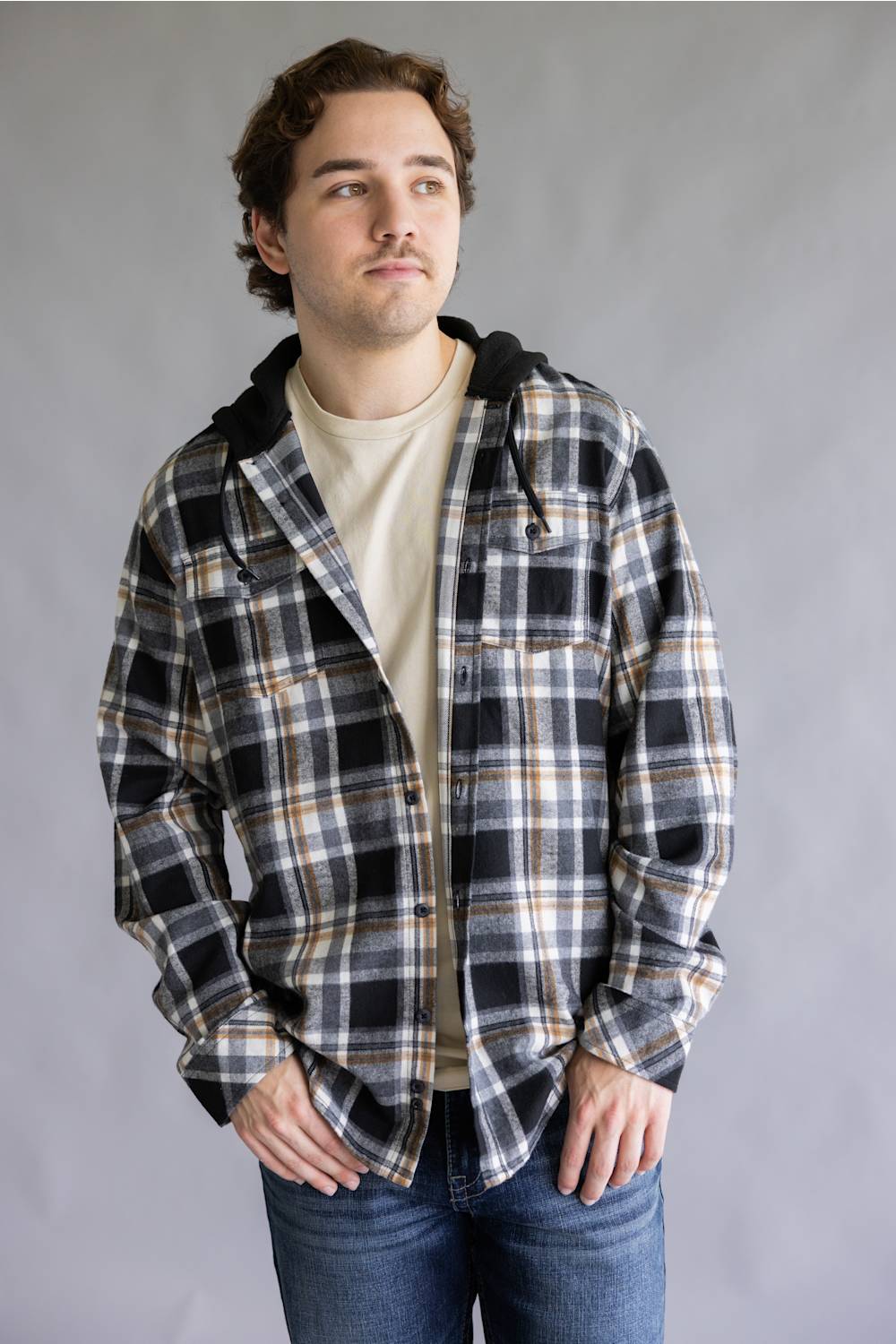 Model wearing the Split Men's long-sleeve hooded flannel shirt in a cream, black, and tan plaid pattern, featuring two chest flap pockets and an attached black hood with drawstrings against a gray studio background.