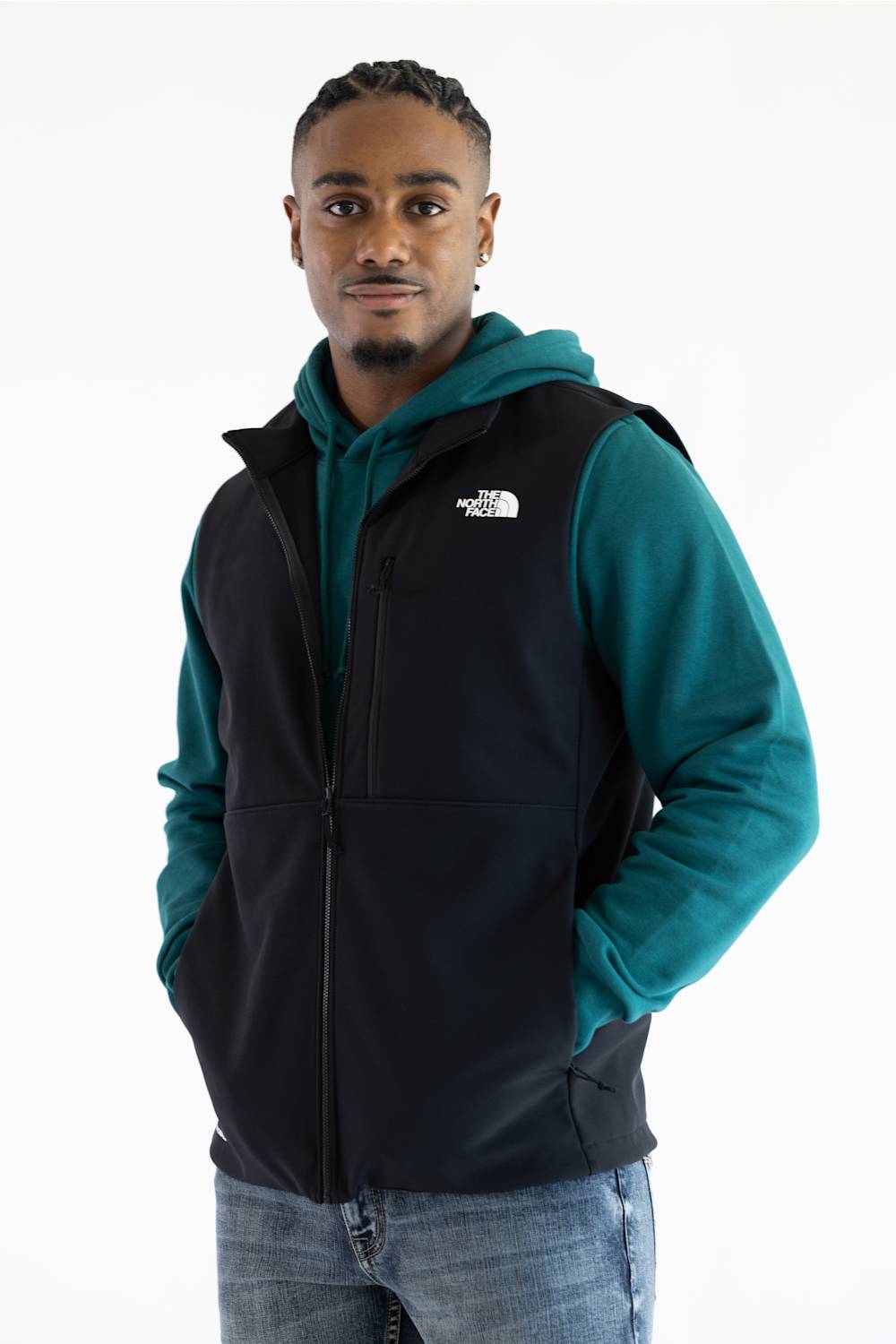 A person wearing a black vest over a teal hoodie, with The North Face logo printed in white on the upper right chest.