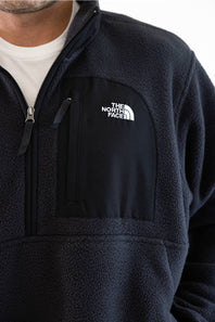 Close-up of a person wearing a dark navy fleece quarter-zip pullover with a white The North Face logo on the left chest, layered over a white t-shirt.
