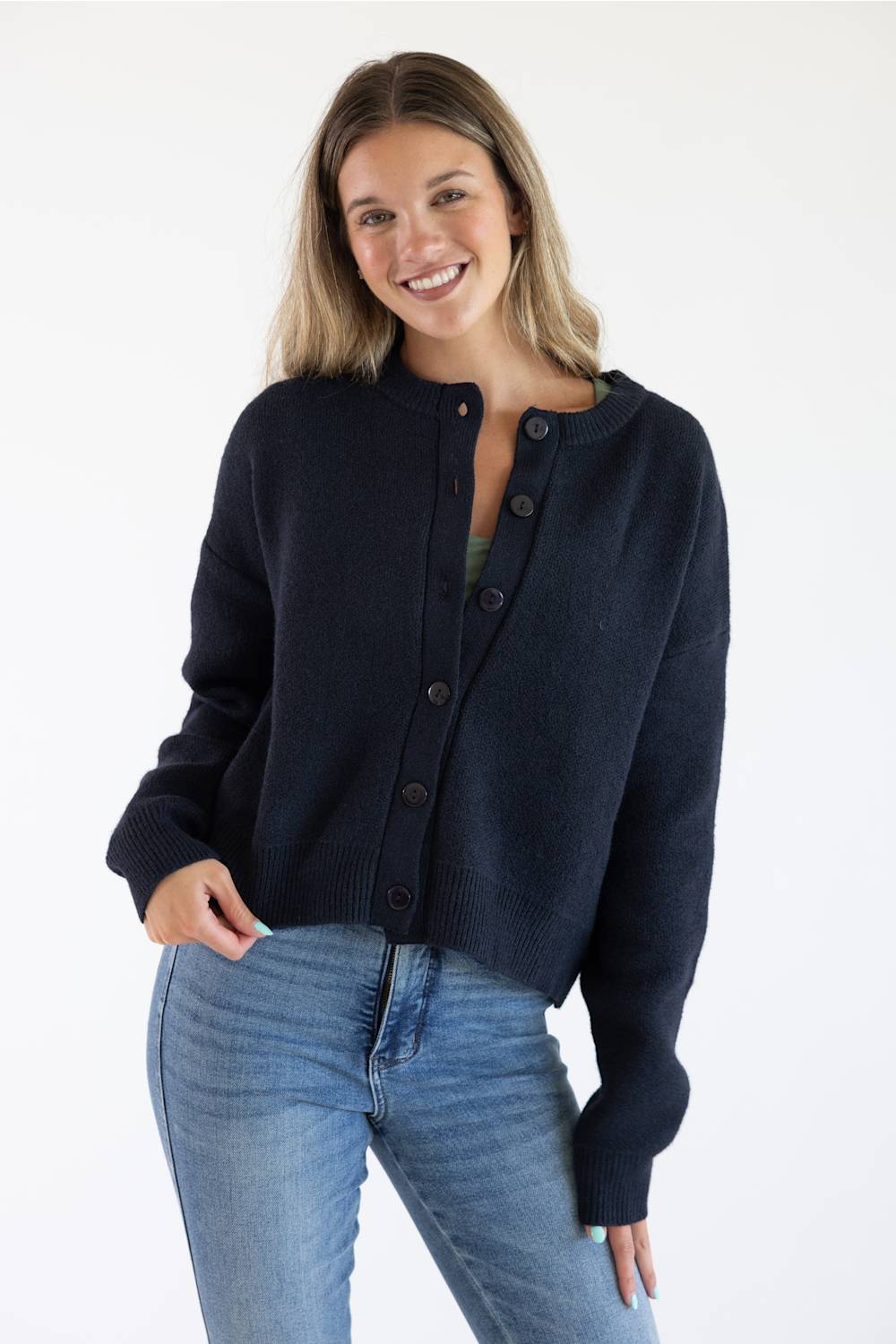 Front view of a female model wearing the Things Between Alyssa Cardigan in Navy, featuring a crew neckline, large front buttons, ribbed hem, and long sleeves paired with blue jeans.