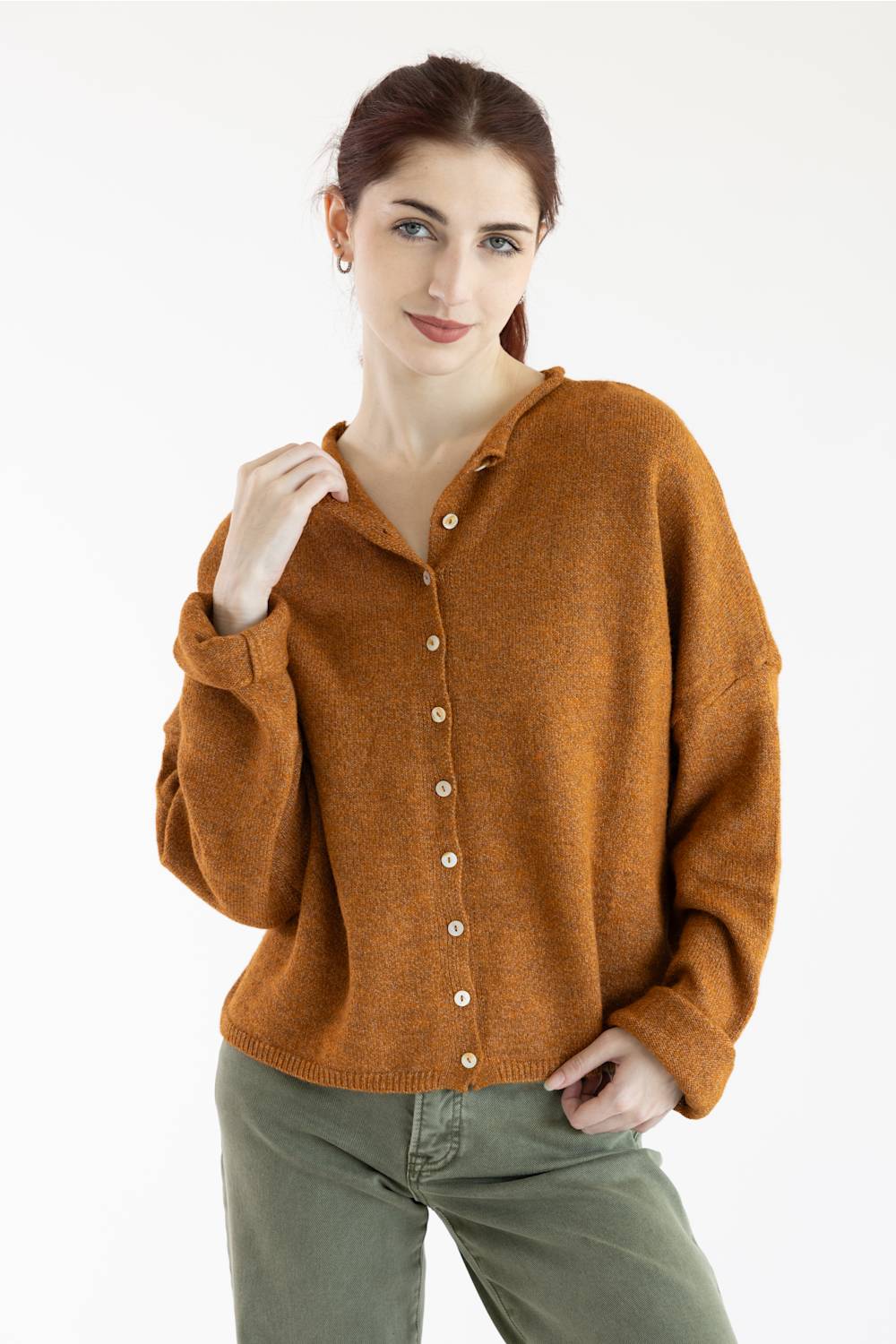 A woman wearing a long-sleeve knit cardigan in a warm rust-orange color with white buttons, paired with olive green pants, against a plain white background.
