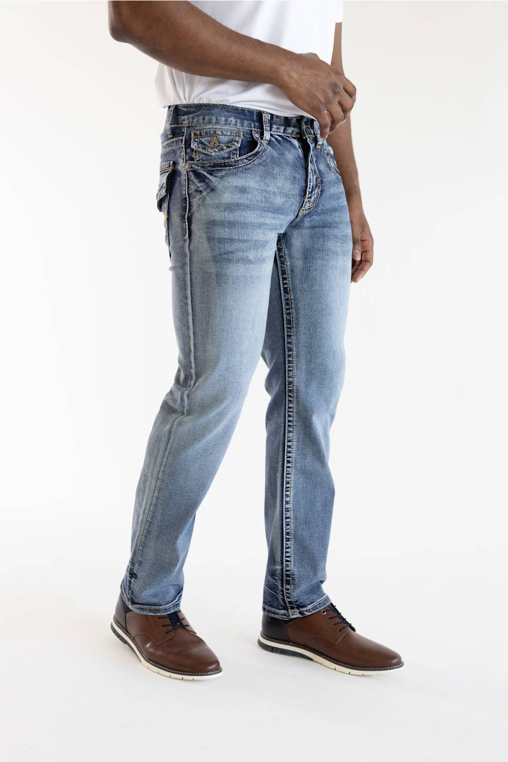A person wearing light blue slim-fit denim jeans with contrast stitching, paired with a white t-shirt and brown leather shoes, shown from the waist down against a plain white studio background.