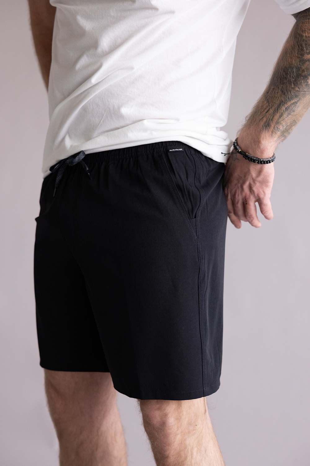 Side view of a person wearing black shorts with a white shirt on a neutral background. The shorts are the Quiksilver Union Amphibian 20" Hybrid Shorts for Men in Black