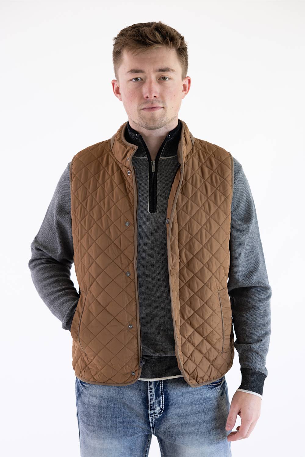 Front view of a model wearing a brown rhombus quilted vest, layered over a gray quarter-zip pullover and blue jeans.