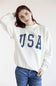 Woman wearing an ivory mock-neck sweatshirt with polka dot USA lettering.
