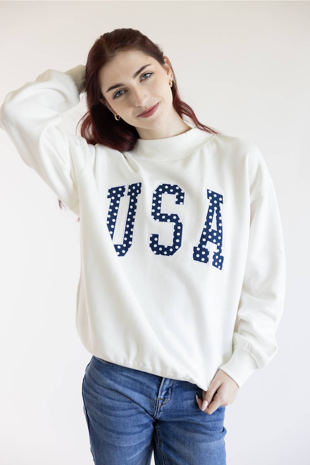 Woman wearing an ivory mock-neck sweatshirt with polka dot USA lettering.