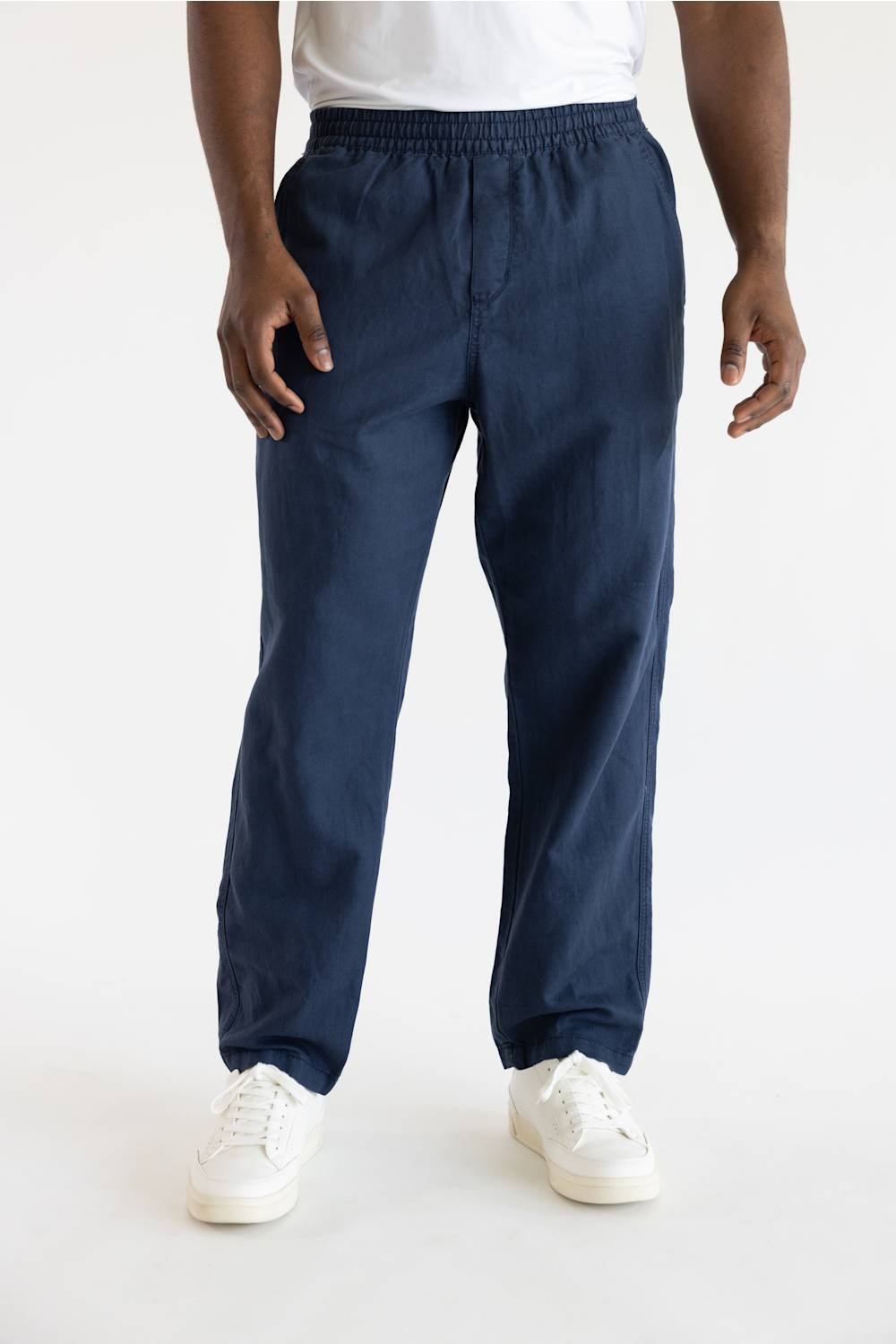 A person wearing navy blue jogger-style pants with an elastic waistband and cuffs, paired with a white top and white sneakers, shown against a plain light background.