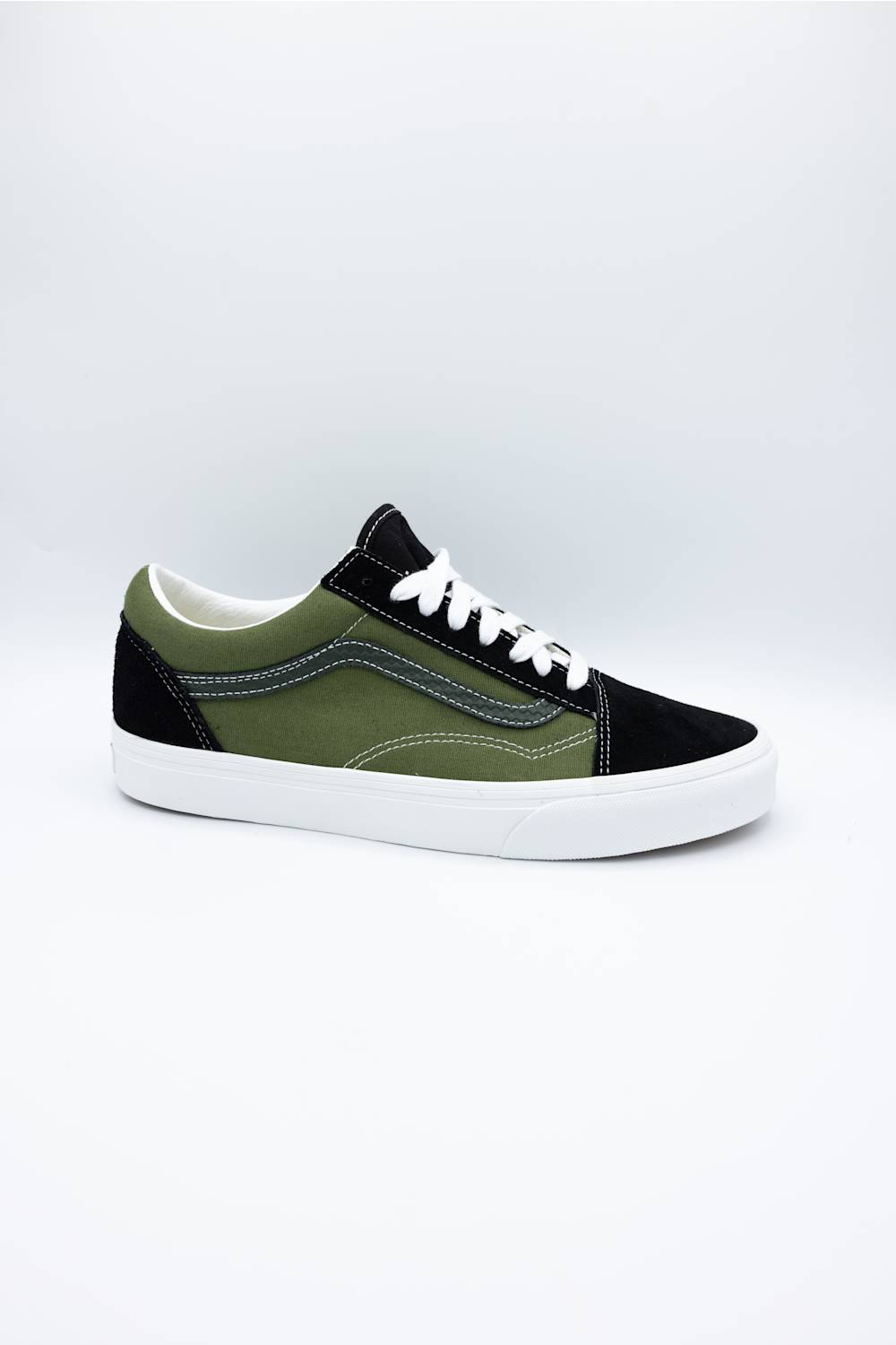 A low-top sneaker with an olive green and black color-blocked design, white laces, and a white rubber sole, photographed on a light gray studio background.