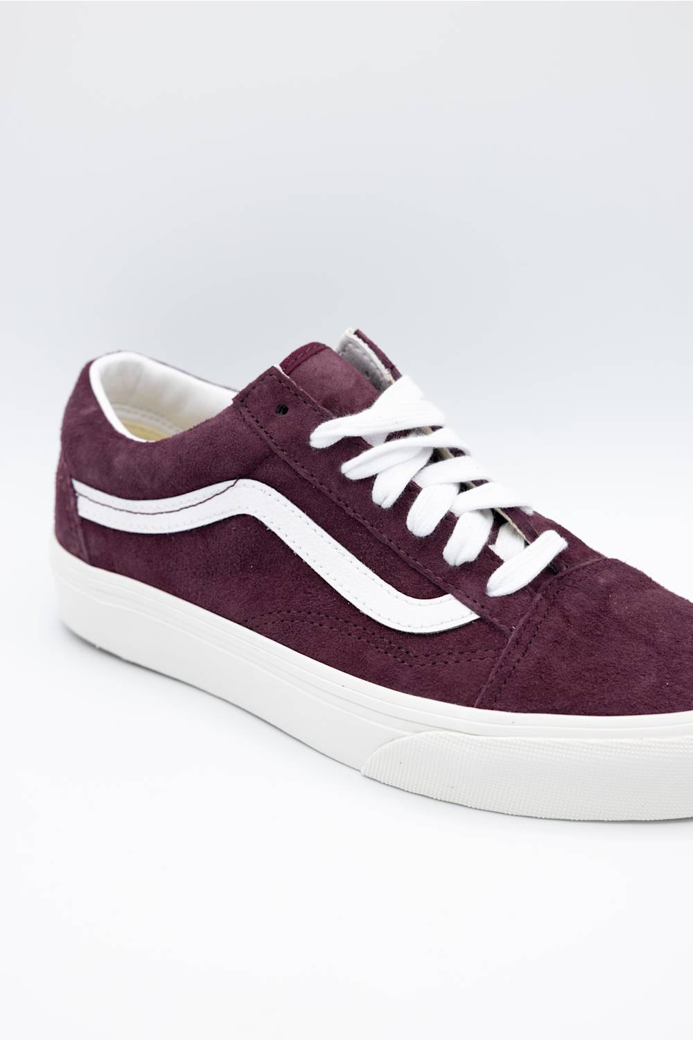 A single Vans low-top sneaker in dark burgundy suede with white laces and a white rubber side stripe and sole, shown on a light gray studio background.