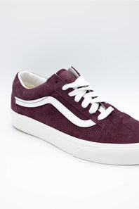 A single Vans low-top sneaker in dark burgundy suede with white laces and a white rubber side stripe and sole, shown on a light gray studio background.