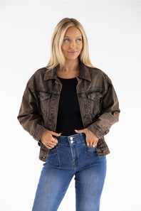A woman modeling a washed brown denim jacket over a black top and blue jeans, standing against a plain white studio background.