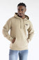 A man wearing a beige pullover hoodie with a drawstring hood and kangaroo pocket, featuring a small black embroidered 'Marsh' logo on the left chest, paired with blue jeans against a plain white background.