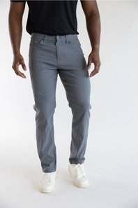 A person wearing slim-fit gray pants, a black t-shirt, and white sneakers, shown from the chest down against a plain light gray studio background.