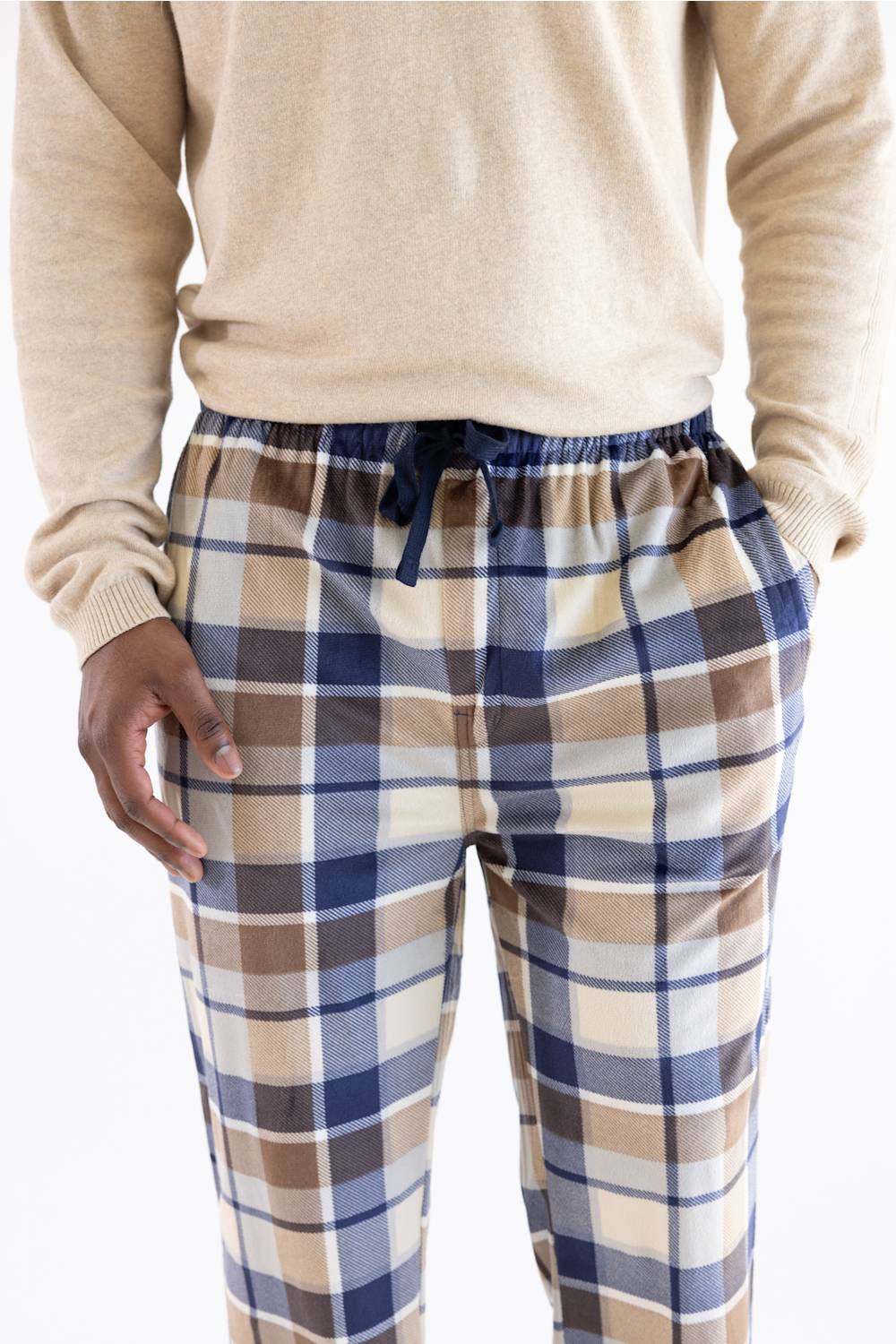 A person wearing plaid lounge pants with a navy drawstring waist, paired with a beige sweater, shown from the chest down against a plain white background.