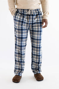 A person wearing blue, white, and beige plaid lounge pants with a drawstring waist, paired with a cream sweater and brown slippers, photographed against a plain white studio background.