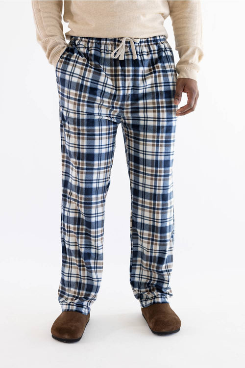 A person wearing blue, white, and beige plaid lounge pants with a drawstring waist, paired with a cream sweater and brown slippers, photographed against a plain white studio background.