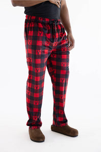 Red and black buffalo plaid pajama pants with a small bear logo printed in each check, modeled with a black t-shirt and brown slippers against a white background.