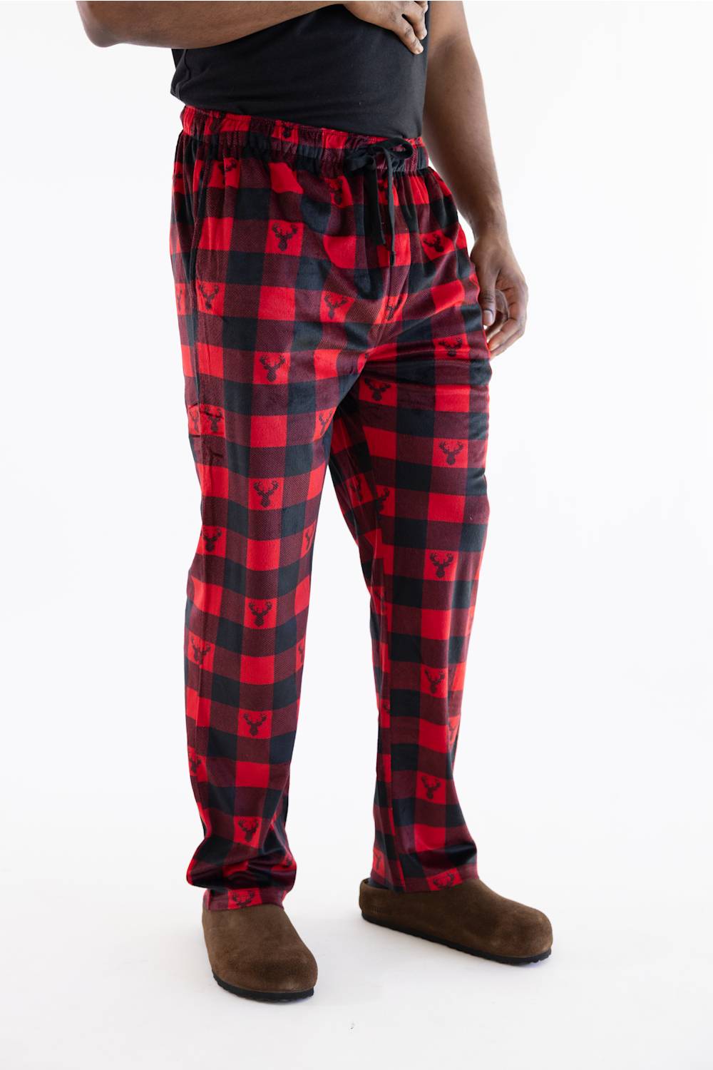Red and black buffalo plaid pajama pants with a small bear logo printed in each check, modeled with a black t-shirt and brown slippers against a white background.