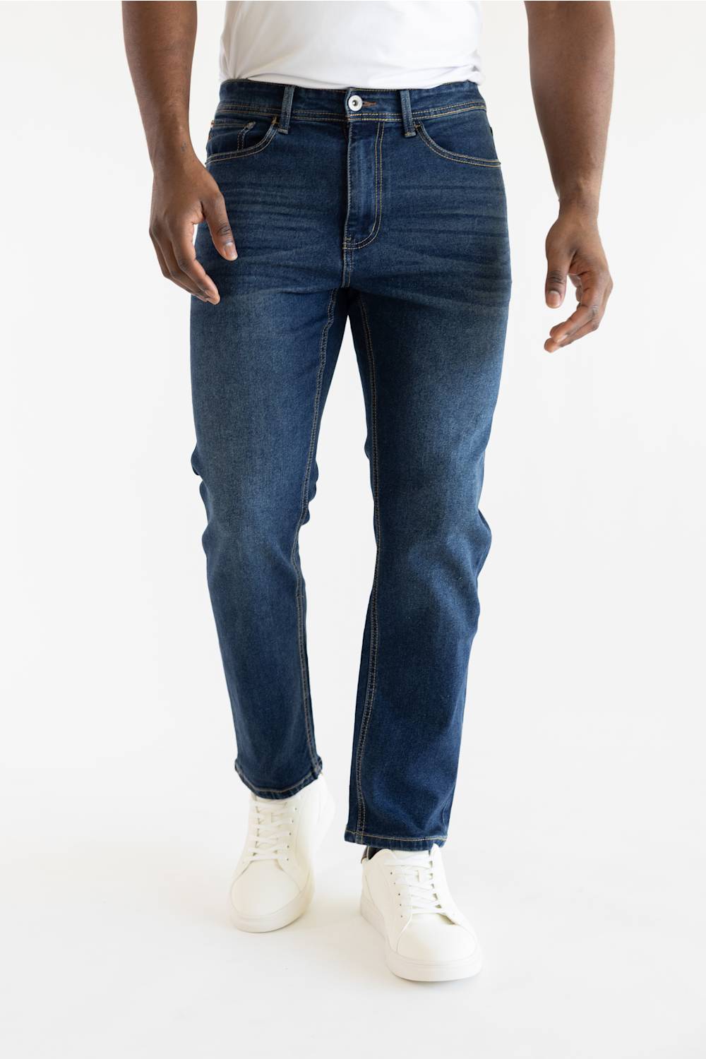 A person wearing dark blue slim-fit jeans with white sneakers, shown from the waist down against a plain white studio background.