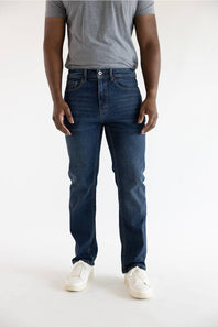 A person wearing dark blue slim-fit jeans, a gray t-shirt, and white sneakers, shown from the waist down against a plain white studio background.
