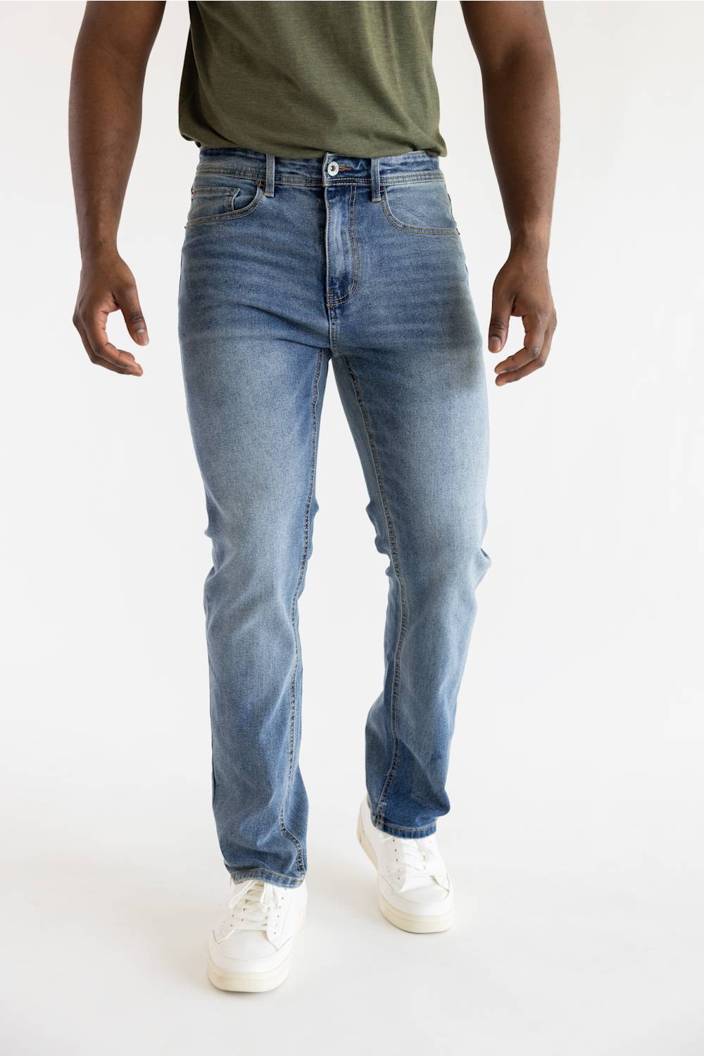 A person wearing light blue slim-fit denim jeans with a faded wash, paired with white sneakers and an olive green shirt, shown from the waist down against a plain white studio background.