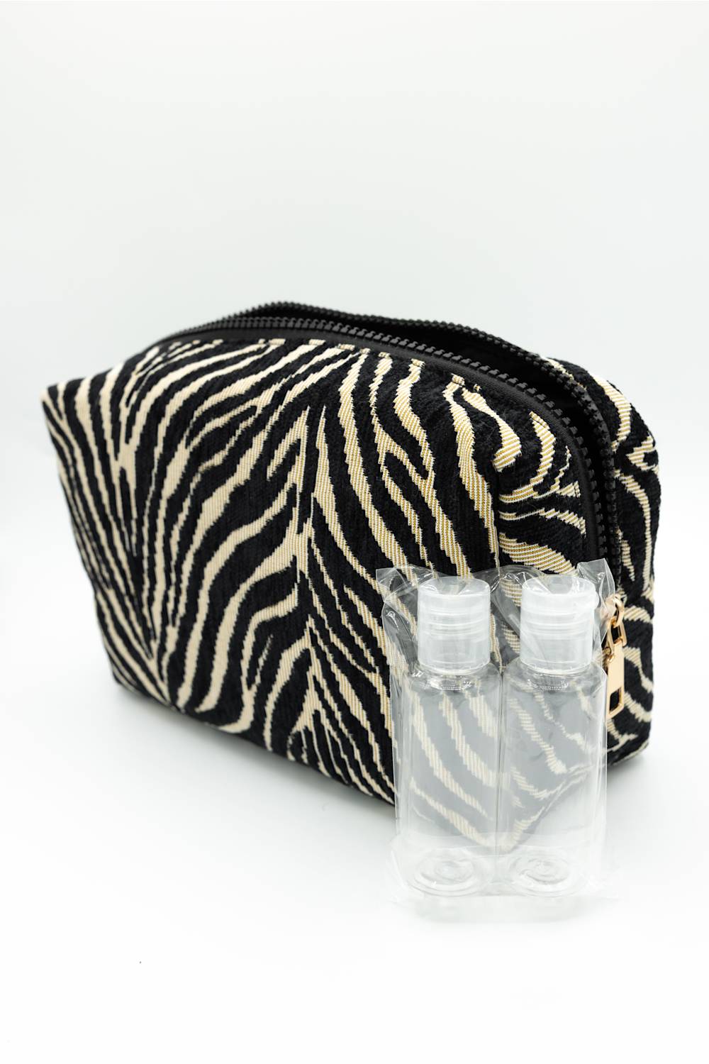A zippered cosmetic pouch with a black and beige zebra print pattern, shown with two small clear plastic hand sanitizer bottles in front on a white background.