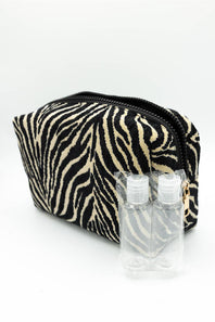 A zippered cosmetic pouch with a black and beige zebra print pattern, shown with two small clear plastic hand sanitizer bottles in front on a white background.