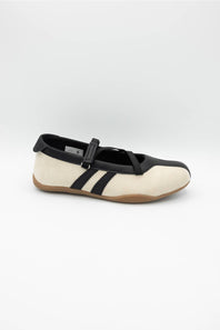 A single Mary Jane style shoe with a cream colored upper, black leather trim and strap, and a brown gum sole, shown against a plain light gray background.