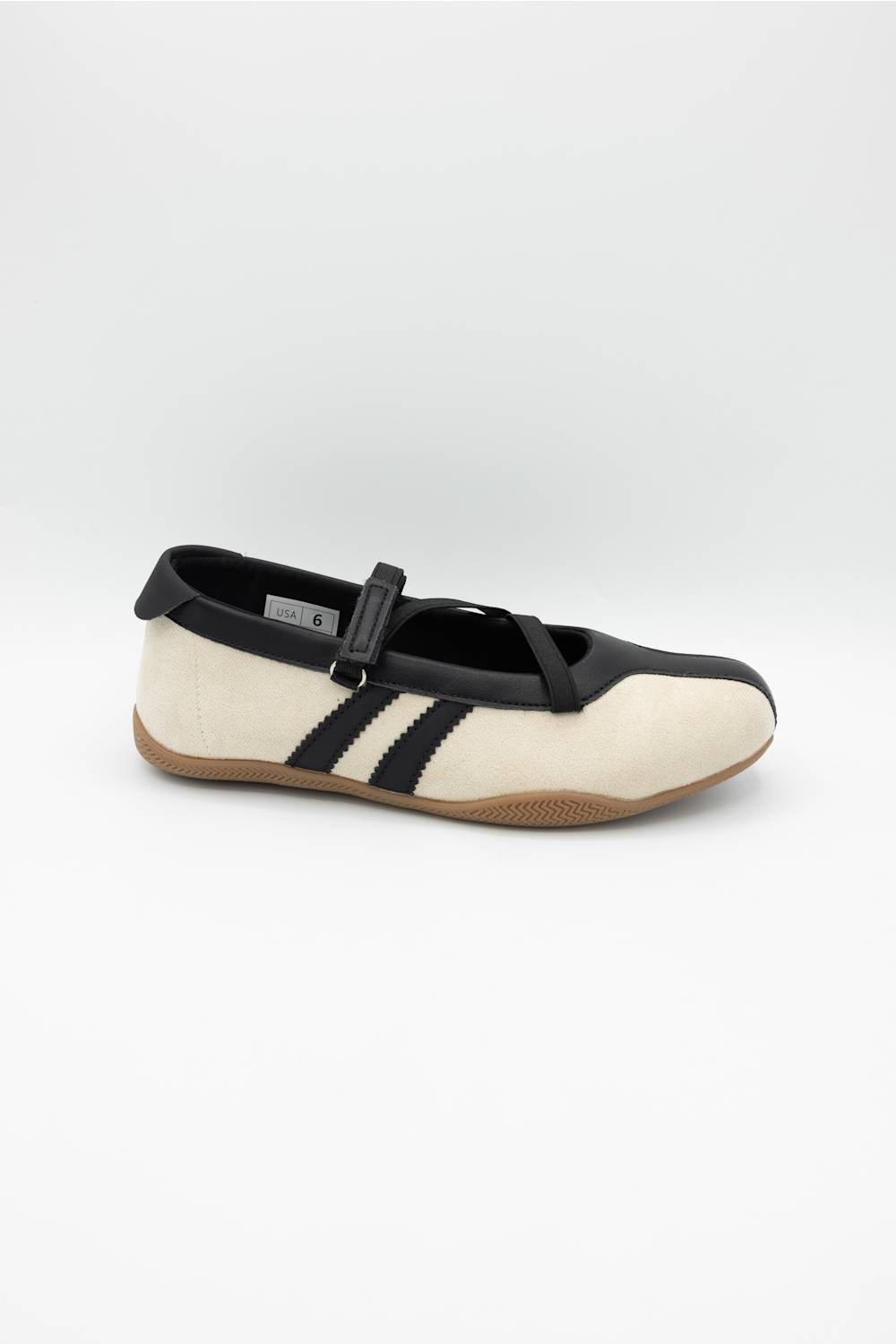 A single Mary Jane style shoe with a cream colored upper, black leather trim and strap, and a brown gum sole, shown against a plain light gray background.