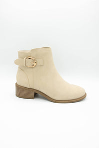 A beige faux-suede ankle boot with a low block heel, a side strap detail, and a gold-tone buckle, shown against a plain white background.