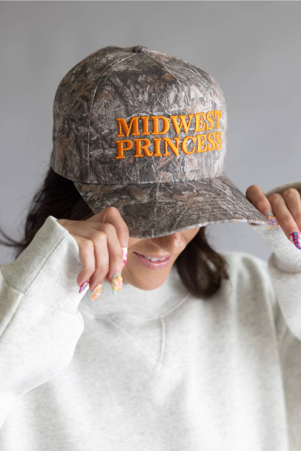 Woman wearing a camouflage cap with 'Midwest Princess' text on a neutral background