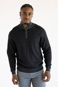 A man wearing a dark charcoal gray quarter-zip sweater with light gray piping details on the collar and cuffs, paired with light gray trousers, against a plain white studio background.