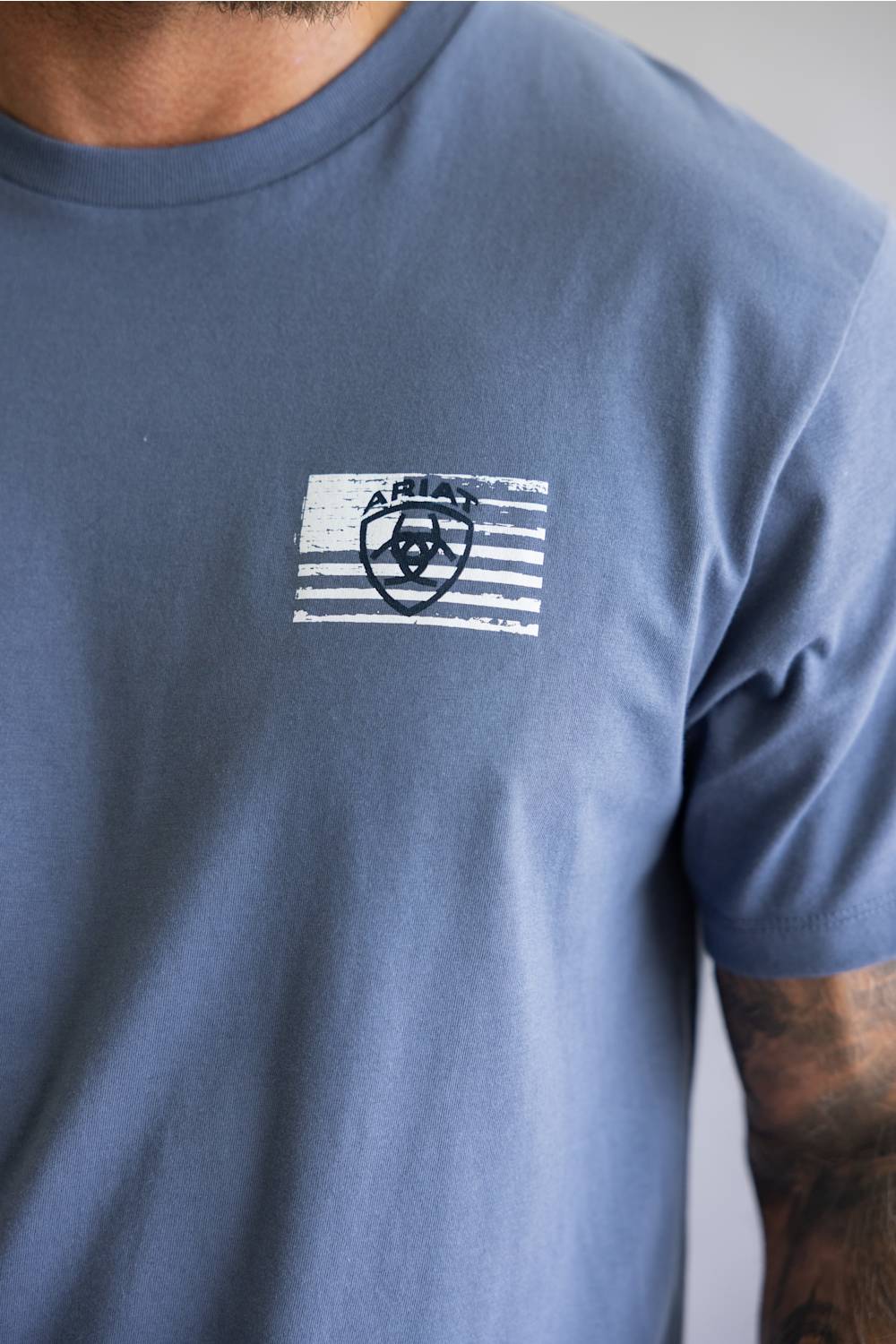 Close-up of a white distressed American flag graphic printed on the chest of a slate blue t-shirt.