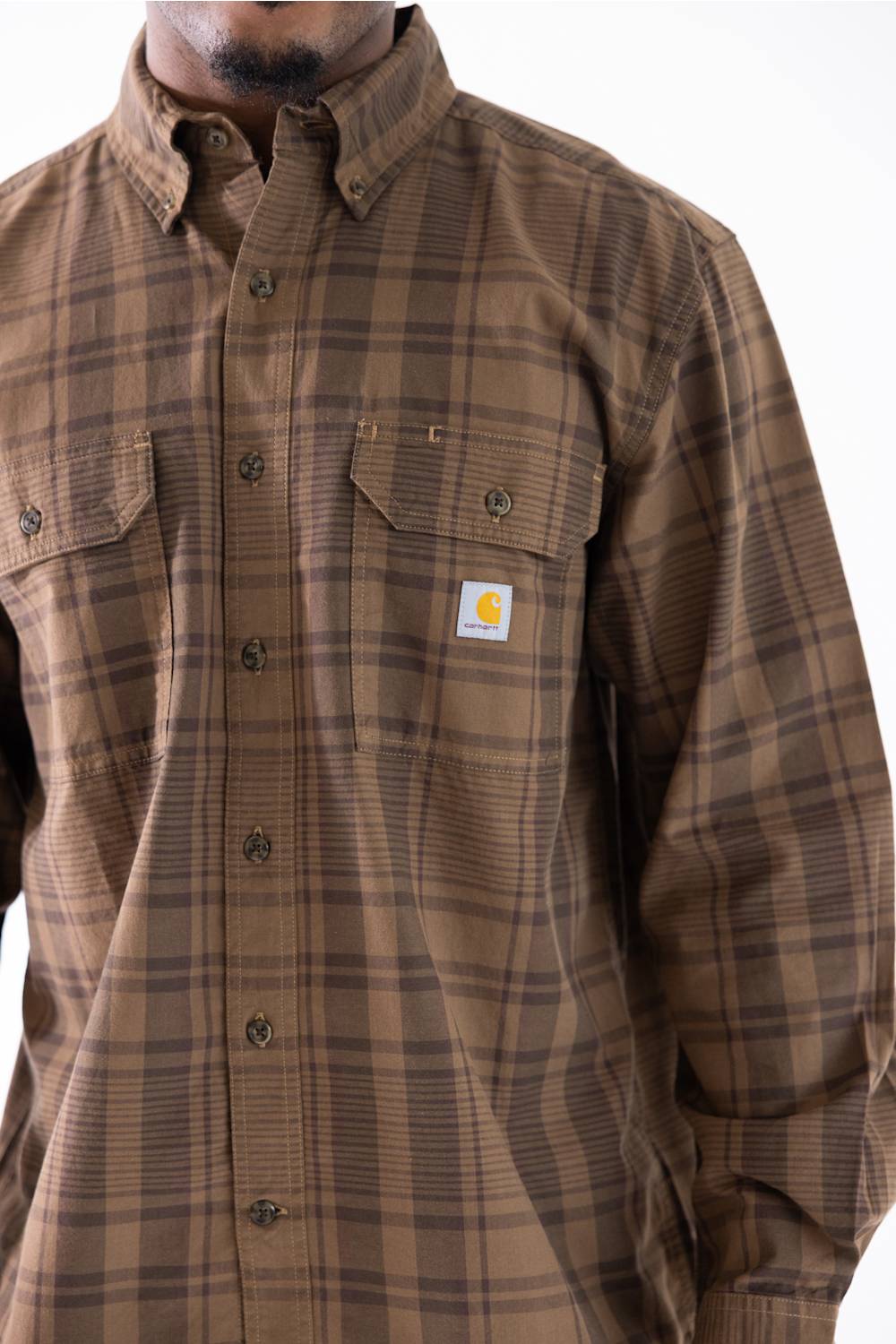 A man wearing a brown and tan plaid button-down shirt by Carhartt, featuring a small white brand patch on the left chest pocket.