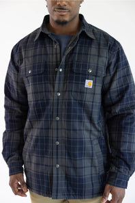 A man wearing a navy blue and gray plaid button-up shirt jacket with two chest pockets and a visible Carhartt logo patch on the left chest, photographed against a plain white background.